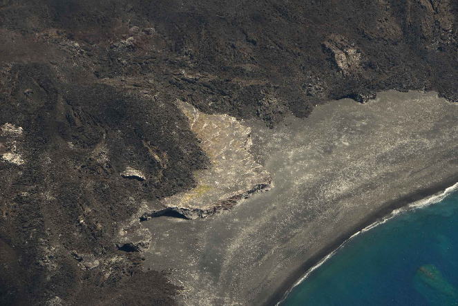 西之島（西ノ島）新島に飲み込まれ、わずかに残る旧西之島（西ノ島）の高台部分　（中央灰白色三日月形の部分）　緑豊かだった旧西之島（西ノ島）、西之島（西ノ島）新島の火山活動によって、一旦失われた緑が復活、三日月形の内側部分、溶岩寄りの辺りから黄緑色の草地が広がっている様子が見られます　（2016年5月20日撮影）