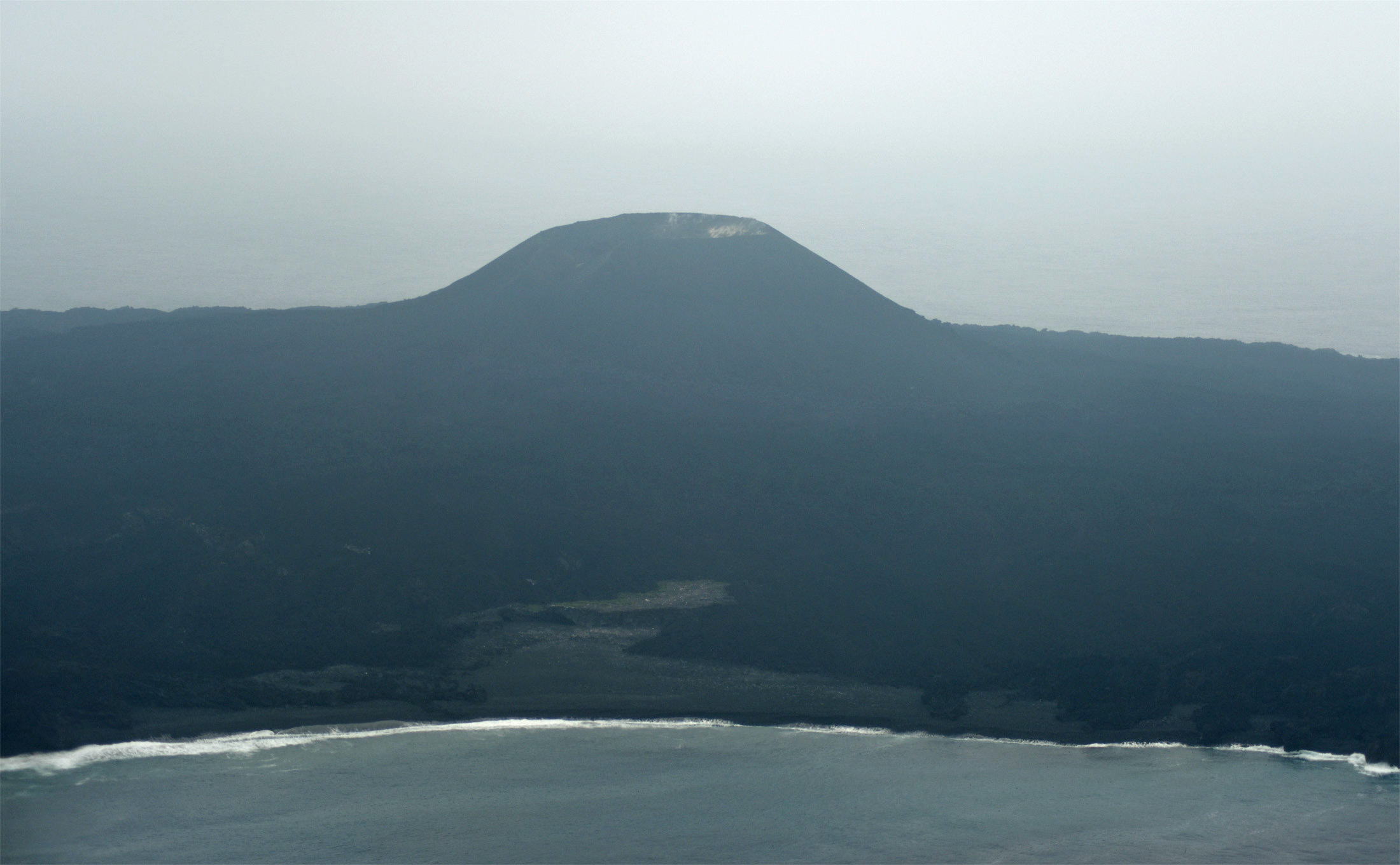 西之島新島に飲み込まれ、わずかに残る旧西之島の高台部分（中央灰白色三日月形の部分）（2018年6月14日撮影）
