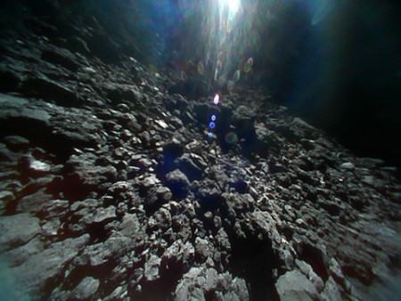 小型探査ロボットが２３日に撮影した小惑星リュウグウの表面の画像。上部の白いものは太陽光＝宇宙航空研究開発機構提供