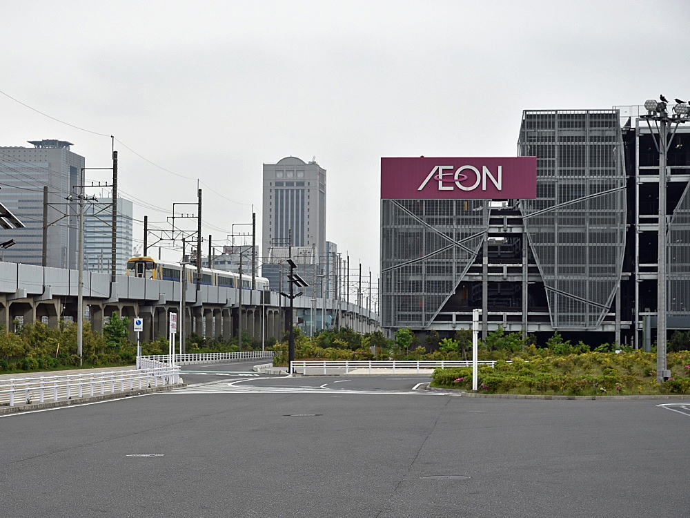 幕張新駅の予定地付近を走るJR京葉線の特急列車。大型の立体駐車場や広いバスターミナル（写真手前）が幕張新都心の交通の現況を物語る。左後方に見えるのは海浜幕張駅北側のオフィスビル群（写真：日経コンストラクション）