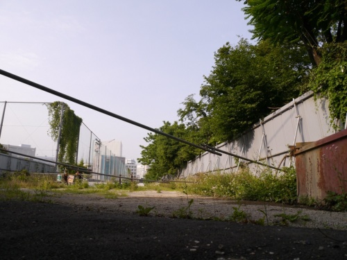 バイパス予定地の南側の様子。写真左は東京都立新宿高校のグラウンドのフェンスで、右は新宿御苑側の仮囲い。新宿高校は04年12月、道路用地を提供するために、学校の敷地内に校舎を新築して移転した。6月上旬に撮影